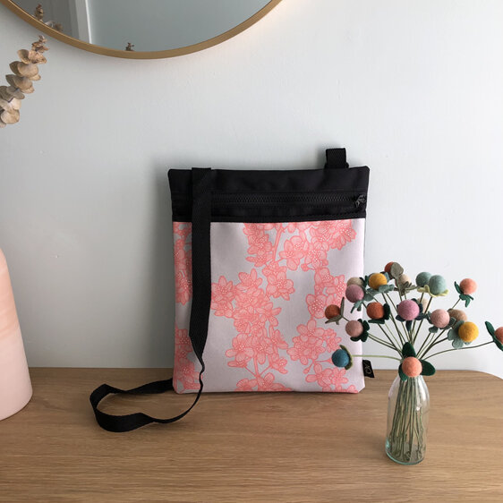 A crossbody flat fabric bag with a pocket in a cherry blossom fabric