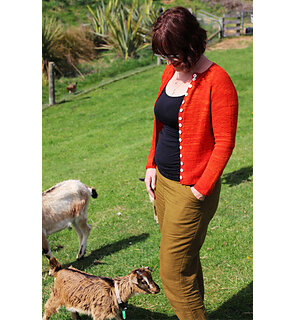image is of a woman wearing an orange cardigan with head down looking at 2 goats