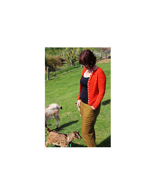 image is of a woman wearing an orange cardigan with head down looking at 2 goats