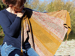 image shows a woman holding a triangle  shawl in golden yellow and red speckles
