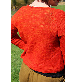 image shows the back of a person wearing a bright orange hand knit cardigan
