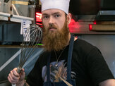 Jeweller in kitchen wearing chefs hat frying pan pendant jewellery design