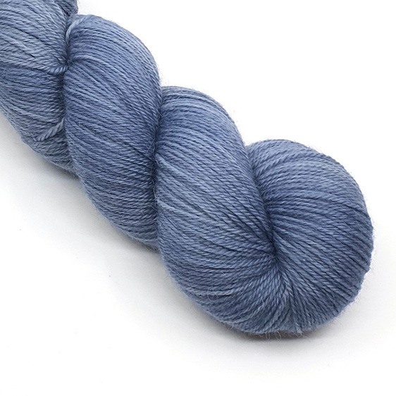 Part skein of yarn in blue grey hues laid diagonally on a white background