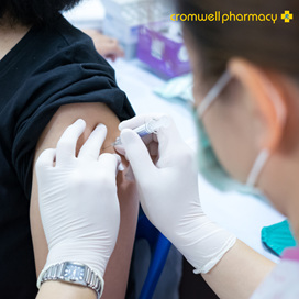 Pharmacist in white gloves jabs the arm of a patient with a needle.