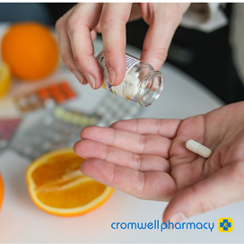 Woman empties pill bottle into hand, orange on bench behind